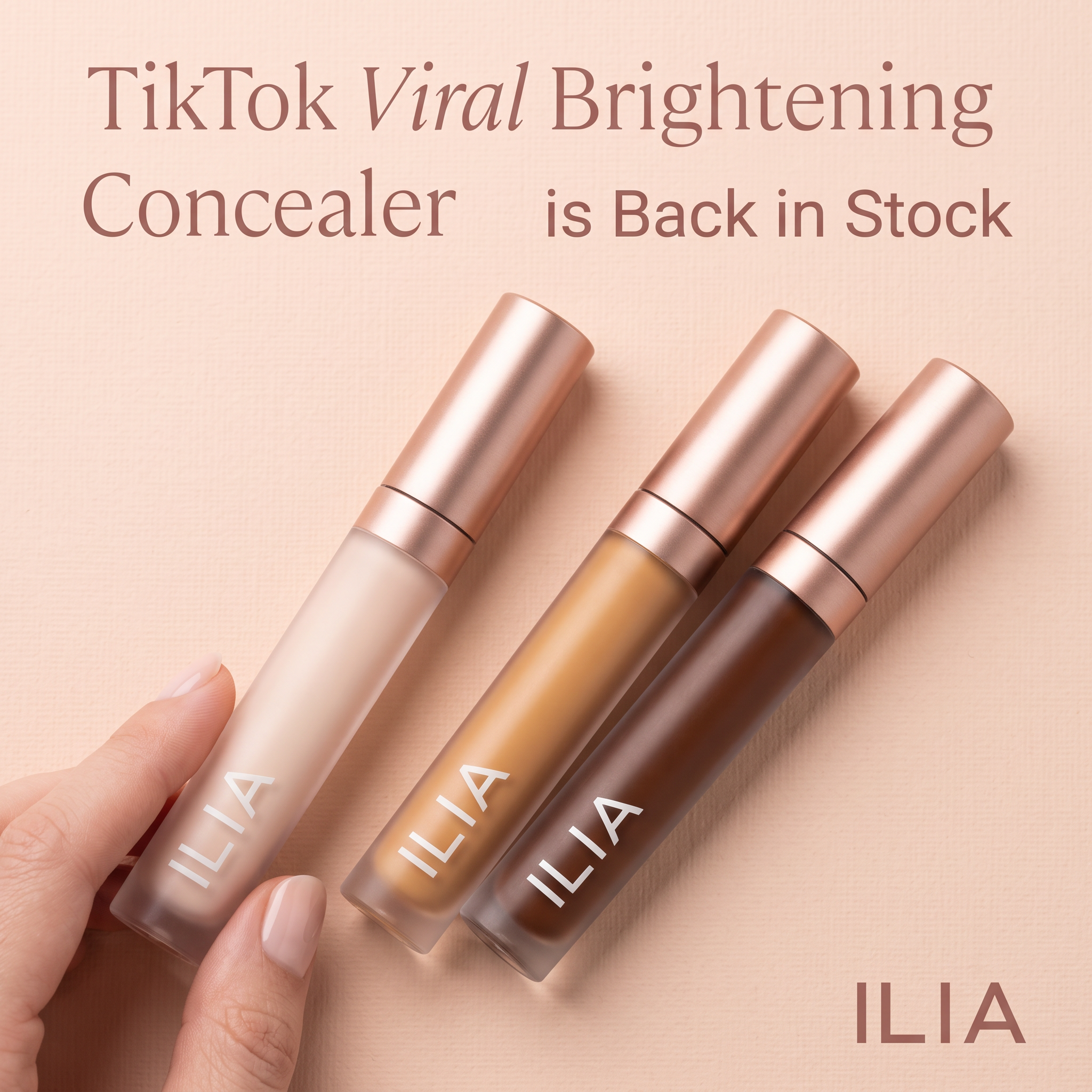 Hand holding three ILIA concealer tubes in light, medium and deep shades with rose gold caps on a peach background