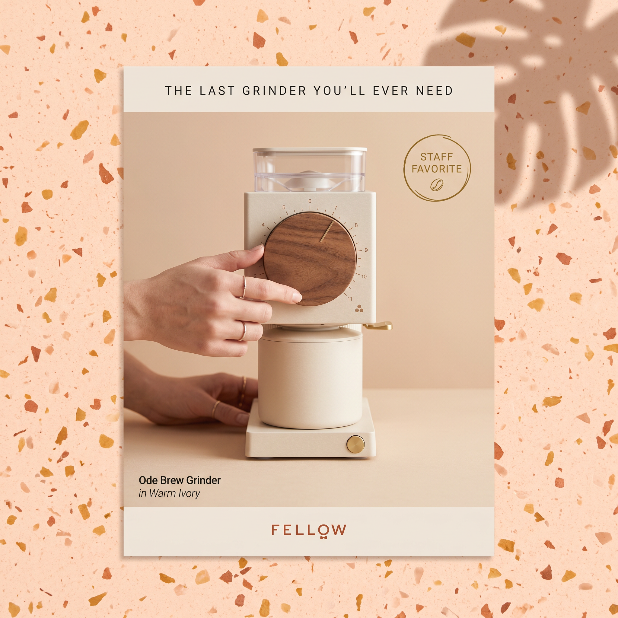 Hand turning the walnut dial of a cream Fellow Ode coffee grinder on a poster set against a peach terrazzo background