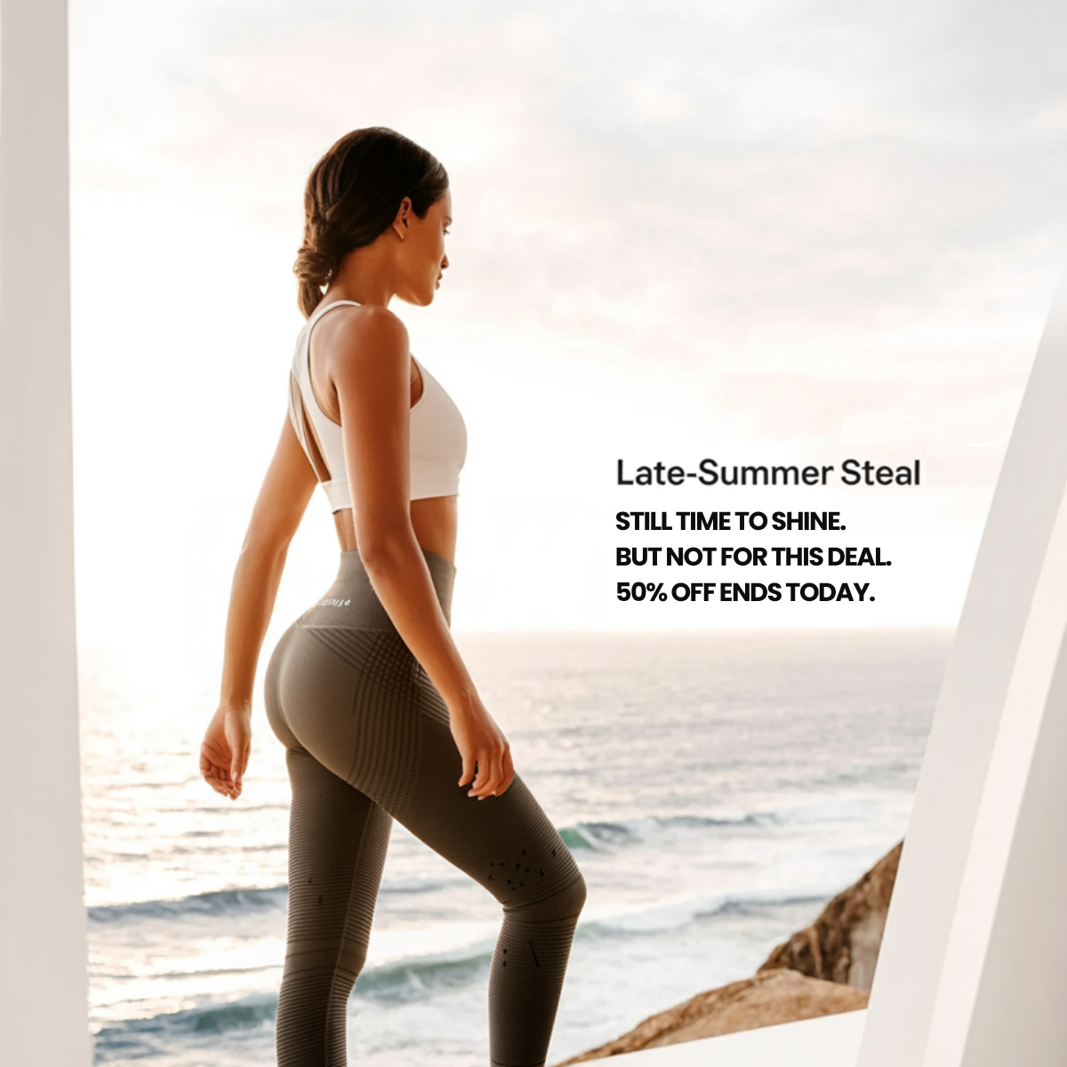 Woman in white sports bra and olive textured leggings looking out at the sea, text Late-Summer Steal 50% off ends today