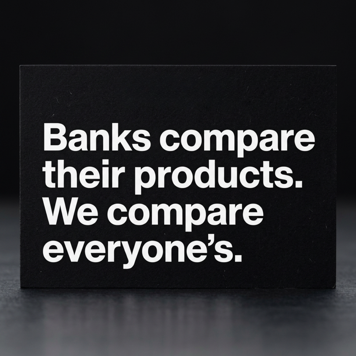 Matte black card on dark surface with white text: Banks compare their products. We compare everyone's.