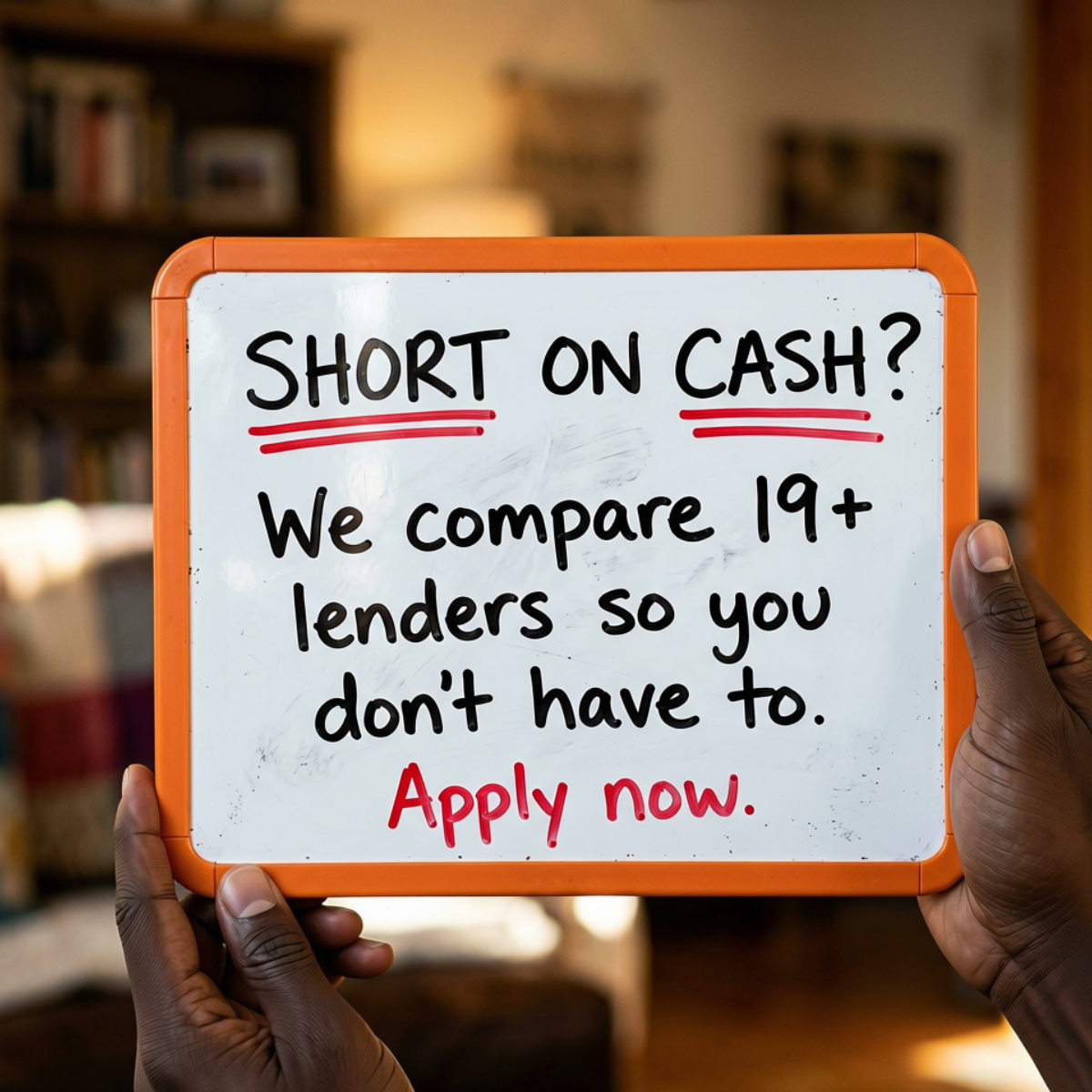 Hands holding an orange-framed whiteboard reading 'Short on cash? We compare 19+ lenders so you don't have to. Apply now.'