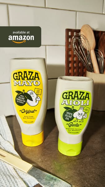 Graza Mayo Original and Garlic Aioli squeeze bottles on a kitchen counter with utensils and an available at Amazon tag
