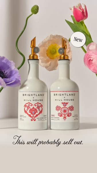 Two Brightland x Hill House olive oil bottles with gold pour spouts surrounded by purple anemone, poppy and pink tulips