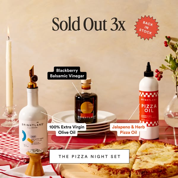 Brightland olive oil, blackberry balsamic and pizza oil on a red table with labelled callouts, pizza and a candle