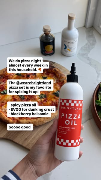 Hand holding Brightland Pizza Oil squeeze bottle in front of homemade pizza with olive oil and balsamic on a marble counter