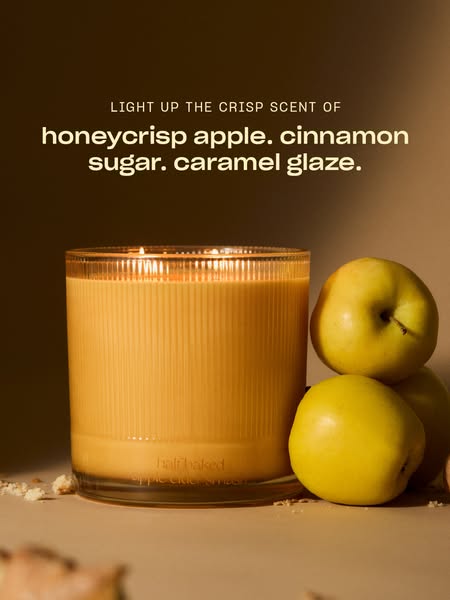 Lit Snif apple cider smash candle in ribbed glass next to stacked yellow apples under warm light with scent notes headline