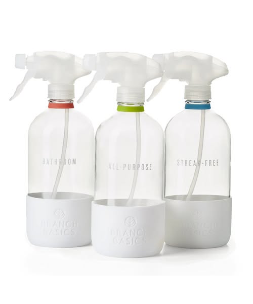 Three refillable glass spray bottles labelled Bathroom, All-Purpose and Streak-Free with white silicone sleeves on white