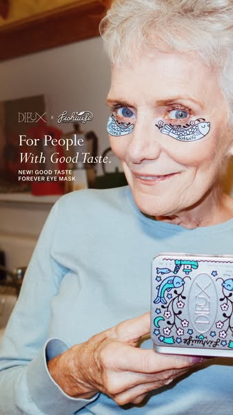 Smiling white-haired woman wearing blue fish-print Dieux eye masks and holding a decorated silver tin