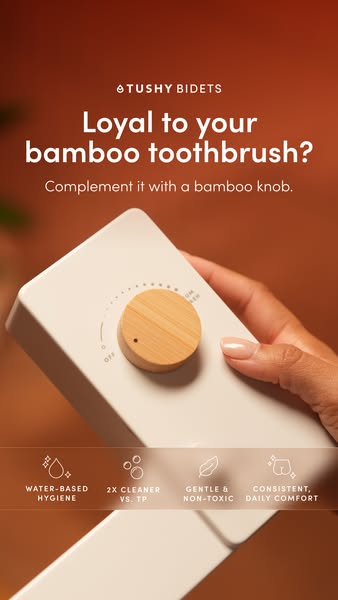 Hand holding a white TUSHY bidet control panel with a bamboo knob on a warm rust background with four icons