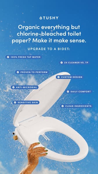 Hand holding a white TUSHY bidet seat against a blue sky with water spray and eight scattered benefit pills