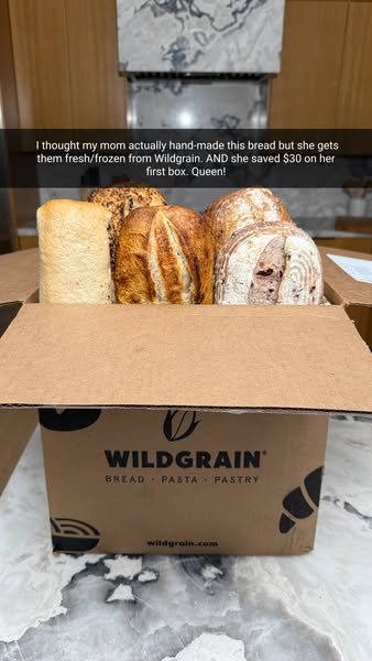 Open Wildgrain delivery box holding four artisan loaves on a marble counter, with a Snapchat-style caption about mom's bread