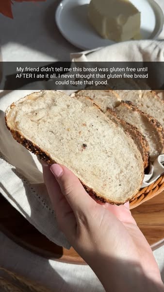 Hand with pink nails holding a slice of seeded gluten-free bread over a basket, with a Snapchat-style caption