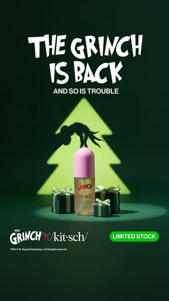 Pink-capped Grinch x Kitsch hair perfume bottle in a spotlight with small green gifts and a glowing Christmas tree silhouette