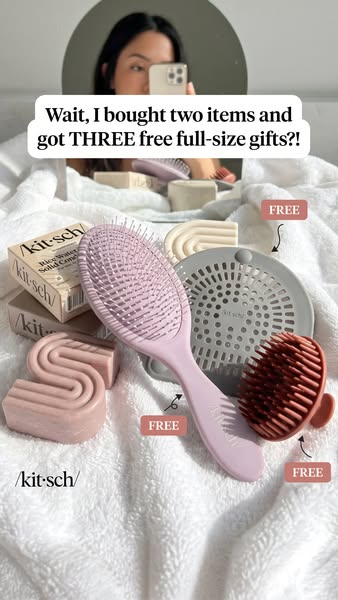 Kitsch shampoo bars, lilac brush, grey drain catcher and rust scalp scrubber on a white towel with three FREE tags