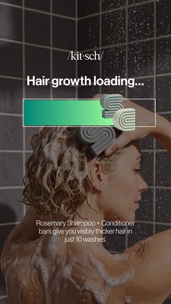Woman lathering curly hair in a dark tiled shower under a green 'Hair growth loading' bar with Kitsch shampoo bars