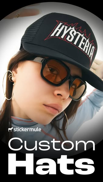 Model with tinted sunglasses and hoop earrings wearing a black trucker cap with red Hysteria flame logo, text Custom Hats