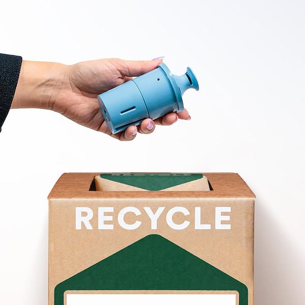 Hand holding a blue plastic filter cartridge above a kraft TerraCycle Zero Waste Box printed with RECYCLE