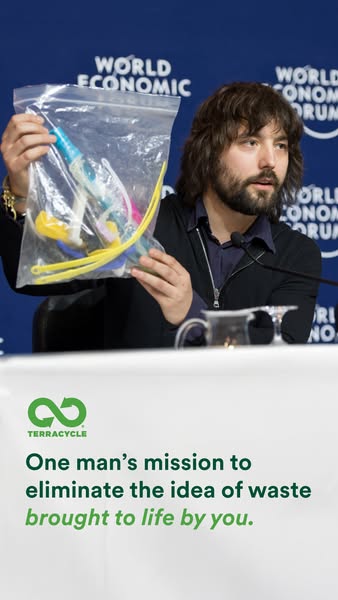 Bearded man at a World Economic Forum press table holding a bag of plastic waste above TerraCycle mission text