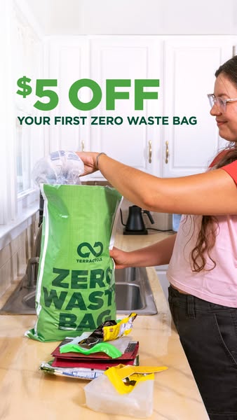 Woman in a white kitchen filling a green Zero Waste Bag with plastic packaging under a green $5 off headline