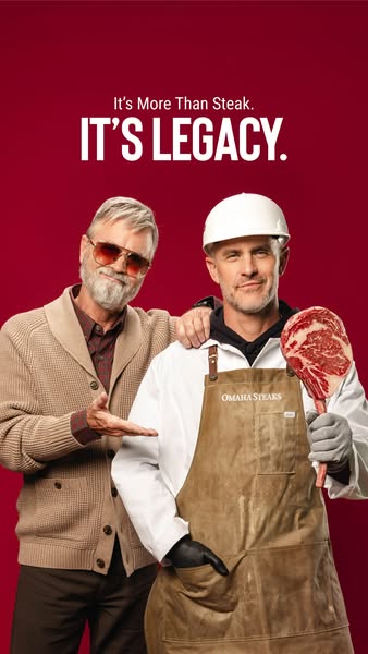 Older man in cardigan and younger butcher in Omaha Steaks apron holding raw tomahawk steak on red background