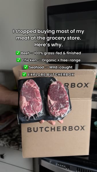 Hand holding a vacuum pack of two raw steaks in front of a ButcherBox delivery box in a home kitchen with emoji checklist