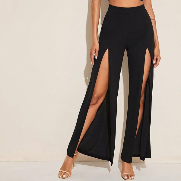 Model wearing black high-waisted wide leg pants with high front slits and nude strappy heels against beige wall
