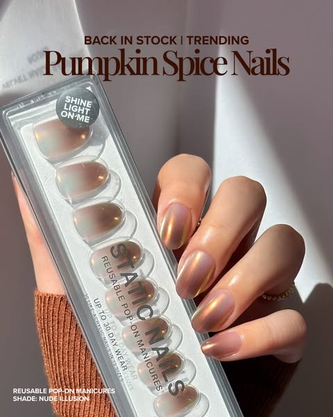 Hand in a rust knit sleeve holding a Static Nails press-on pack, wearing copper-chrome Nude Illusion nails