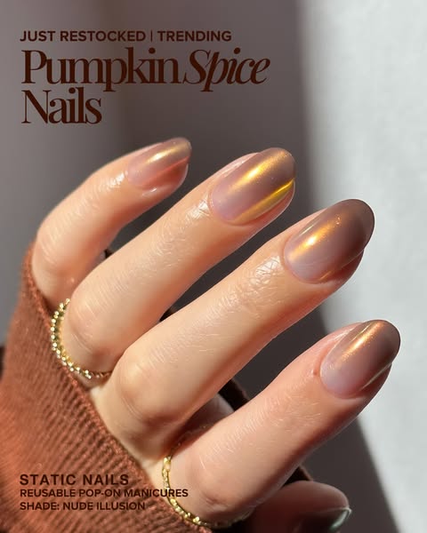 Close-up of a hand in a rust knit sleeve wearing nude press-on nails with copper-gold chrome in warm sunlight