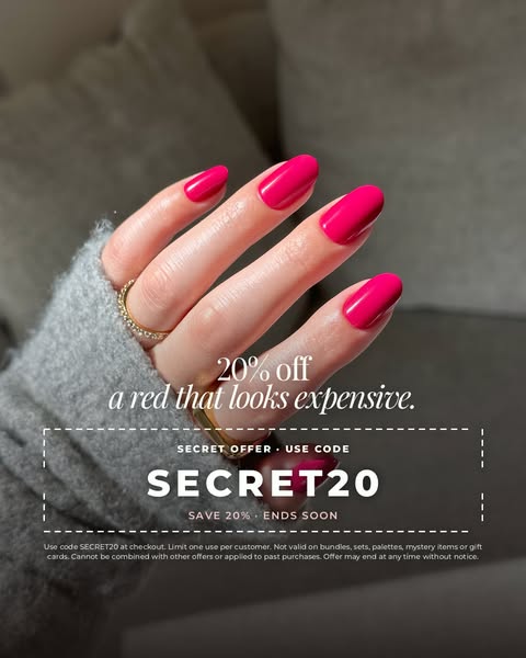 Hand in a grey knit sleeve with glossy pink-red press-on nails on a grey sofa, above a coupon box with code SECRET20