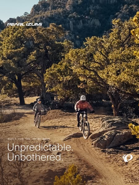 Two mountain bikers on a dusty desert trail among pine trees with headline Unpredictable. Unbothered.
