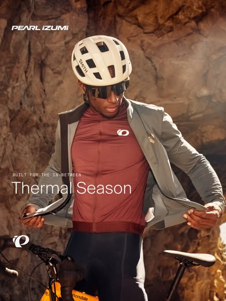 Cyclist pulling a grey jacket over a burgundy jersey in front of a rock wall with headline Thermal Season