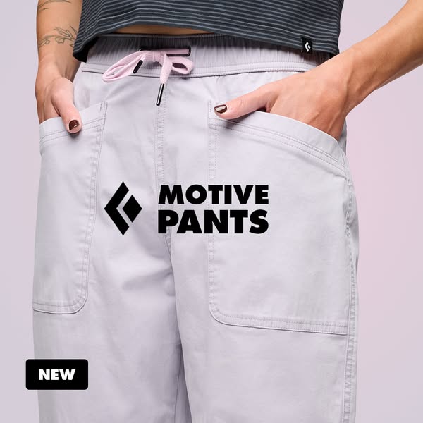 Close-up of woman in light lilac Black Diamond Motive Pants with hands in pockets, bold black logo and NEW badge
