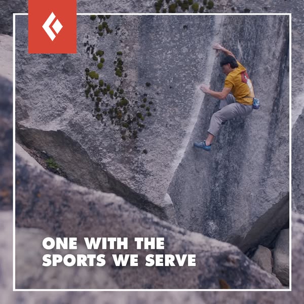 Boulderer in yellow shirt climbing a tall granite boulder with Black Diamond logo and slogan One With the Sports We Serve
