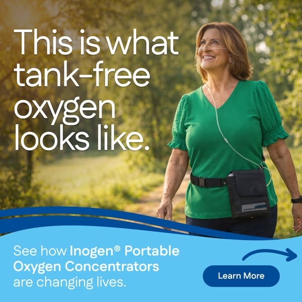 Smiling woman in a green top walks on a sunny forest path wearing an Inogen portable oxygen concentrator on her waist