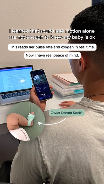 Dad at a desk checks the Owlet app on his phone, with an inset of a baby's foot wearing the green Owlet Dream Sock