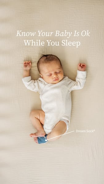Top-down photo of a sleeping baby in a white bodysuit on a cream sheet, wearing a blue Owlet Dream Sock on one foot
