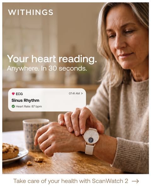 Mature woman at a kitchen table touching her Withings ScanWatch 2 to take an ECG, card showing sinus rhythm and 87 bpm.