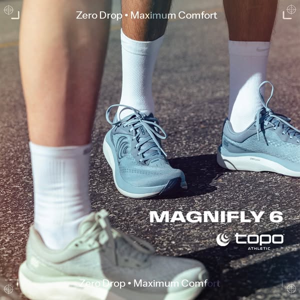 Low-angle shot of runners' legs in white socks and light blue Topo Magnifly 6 shoes on asphalt with Zero Drop text