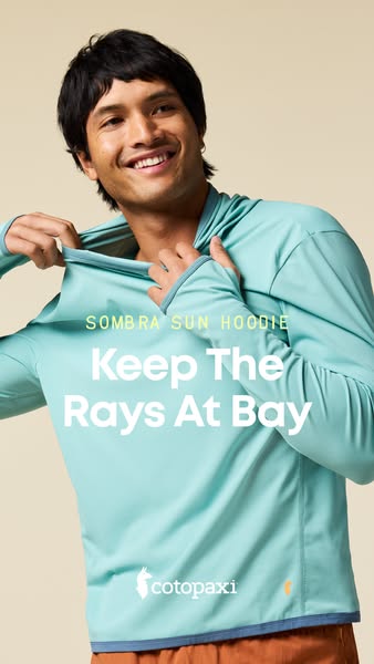 Smiling man pulling up the collar of a seafoam green Cotopaxi Sombra sun hoodie on a beige background
