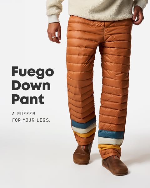 Model wearing rust orange Cotopaxi Fuego down pants with striped hems and brown clogs on a white background