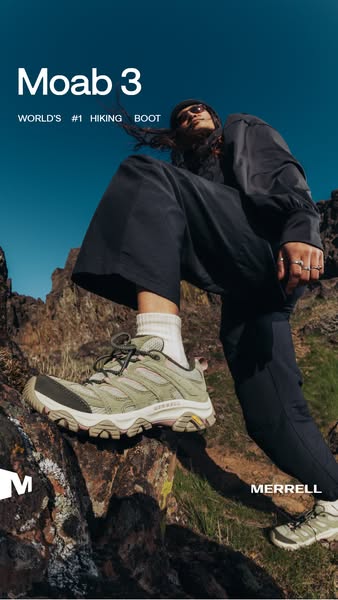 Hiker in dark wide-leg trousers and sunglasses steps onto a rock in sage green Merrell Moab 3 shoes under a deep blue sky